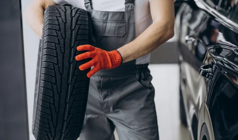 A man in overalls stands holding a tire, preparing for a tire change.