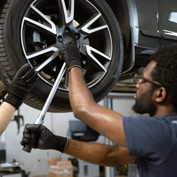 Two men collaborating to change a car tire, demonstrating teamwork and mechanical skills in an outdoor setting.