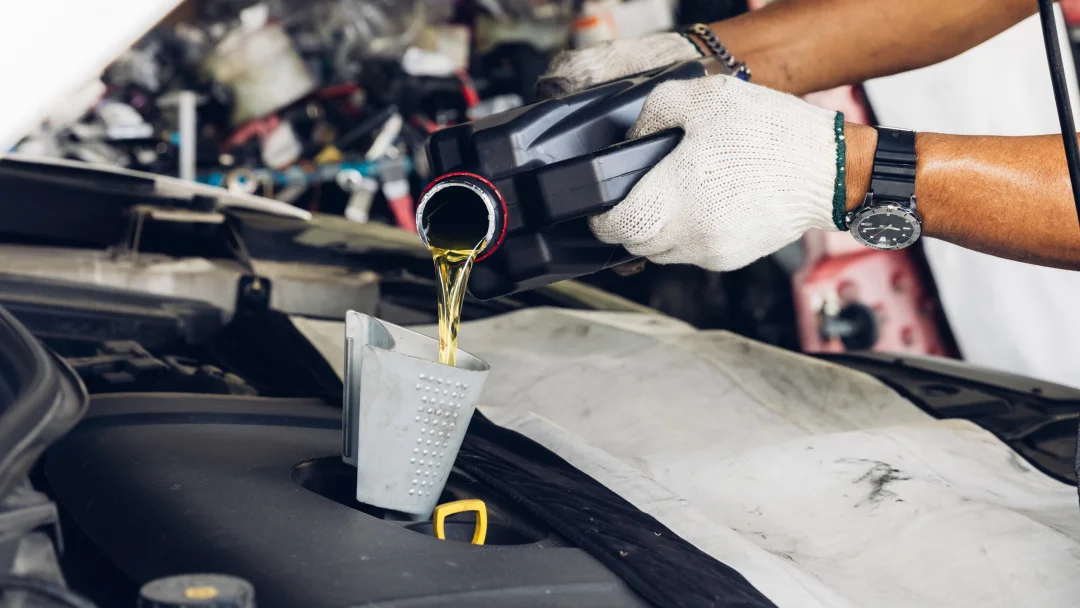 A person performing an oil change by pouring oil into a car engine for maintenance.