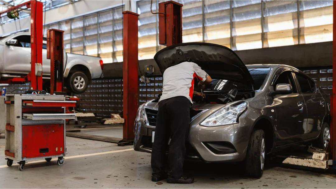 A man performs car maintenance in a garage, focused on repairing the vehicle.