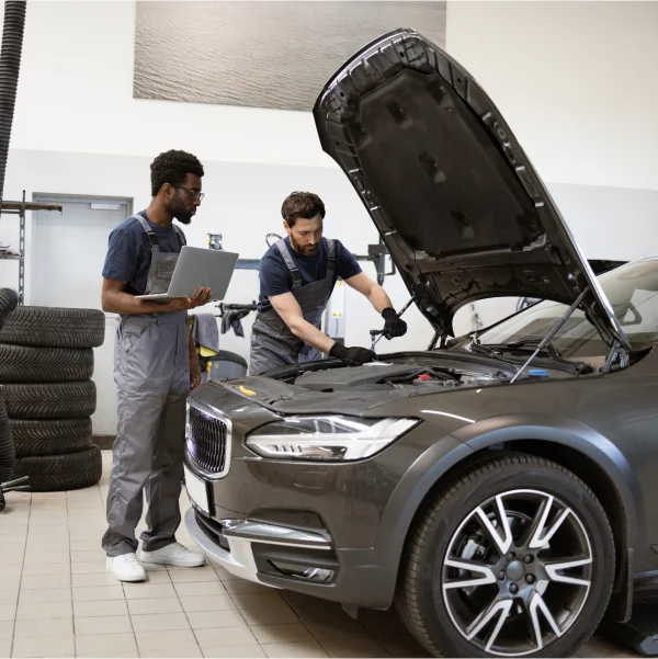 A man in a grey shirt performing car maintenance tasks in a garage setting.