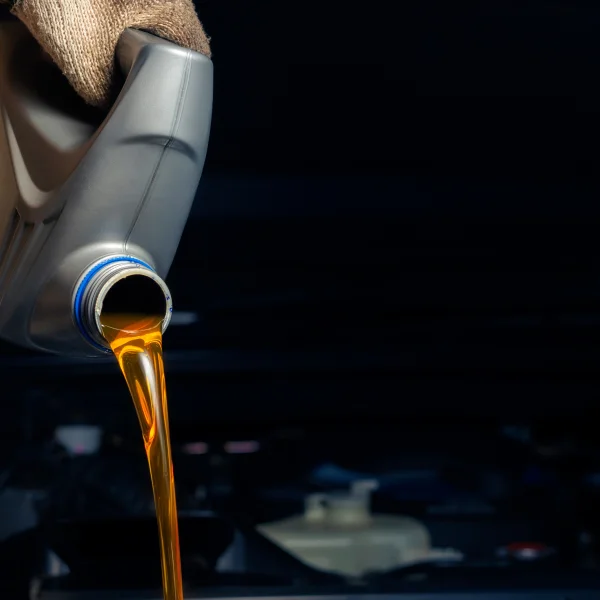 A person performing an oil change by pouring oil into a car engine for maintenance.