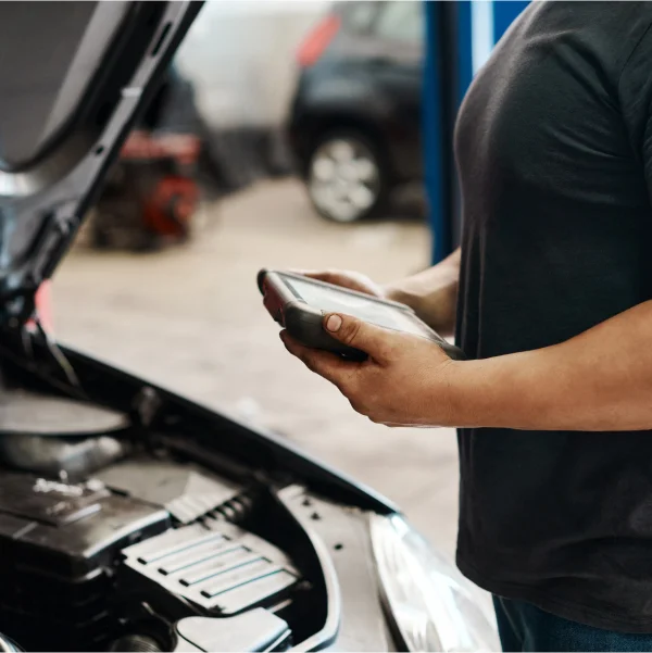 A man examines his car while holding a tablet, focusing on car maintenance information.