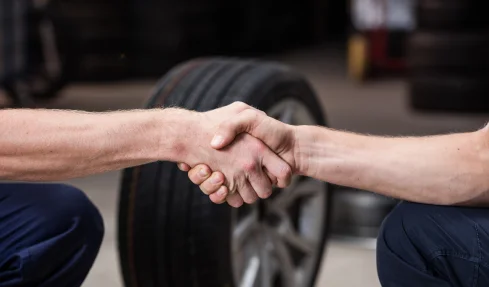 Two men shaking hands over a tire, symbolizing a successful tire purchase agreement.