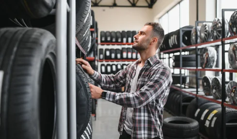 A man examines various tires in a store, contemplating his purchase options for new tires.