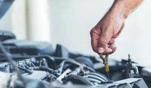 A mobile mechanic inspects a car's oil while holding a wrench, ensuring optimal vehicle performance.